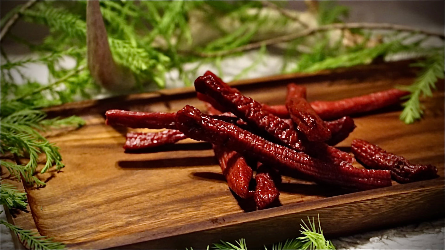 Beef jerky set on a cutting board with cypress branches in the background.